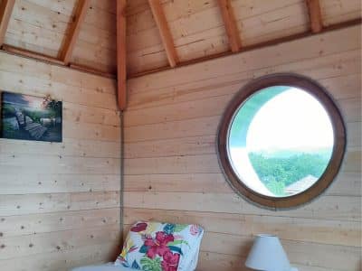 Chalet en bois avec lit floral et grande fenêtre ronde offrant une vue panoramique.