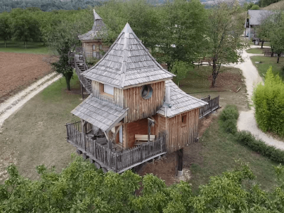 Cabane en bois perchée, avec toit en ardoise, entourée de verdure en Auvergne-Rhône-Alpes.