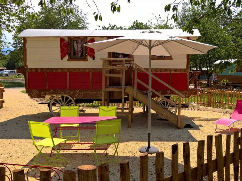 Roulotte colorée avec terrasse, parasol et mobilier extérieur en Auvergne-Rhône-Alpes.