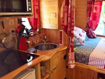 Cabane en bois cosy avec kitchenette et lit douillet, décorée de tissus colorés.
