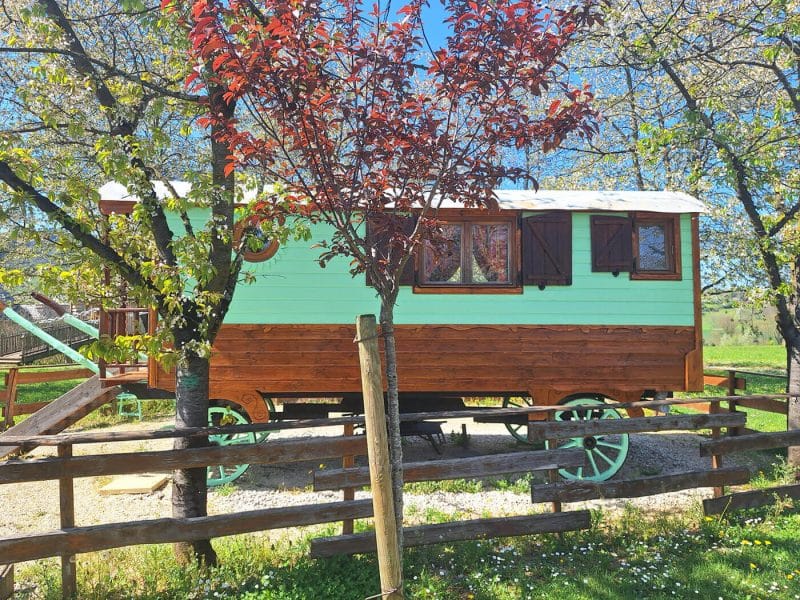 Charmante roulotte en bois, entourée darbres fleuris, idéale pour un séjour insolite.