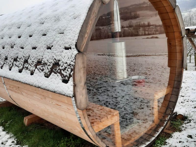 Hébergement insolite en forme de tonneau, entouré de neige et offrant une vue panoramique.