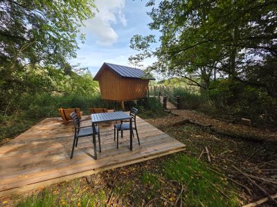Cabane perchée en bois avec terrasse en bois, entourée de verdure luxuriante.