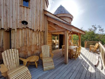 Cabane en bois perchée avec terrasse ensoleillée et mobilier en bois.