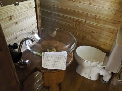 Salle de bain dun hébergement insolite en bois, avec lavabo en verre et décor chaleureux.