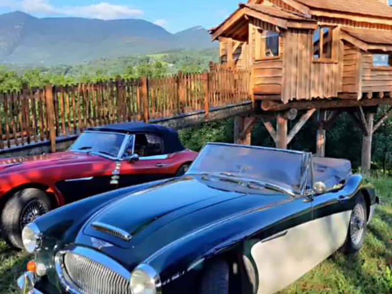 Cabane perchée en bois avec voitures anciennes, vue sur les montagnes.