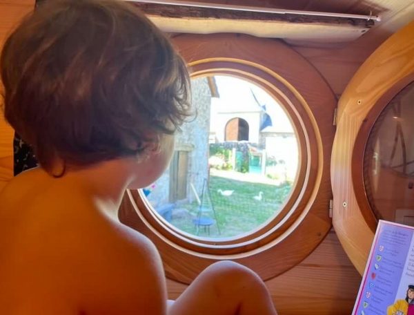 Cabane en bois avec vue ronde sur le jardin et des poules. Enfant contemplatif à lintérieur.