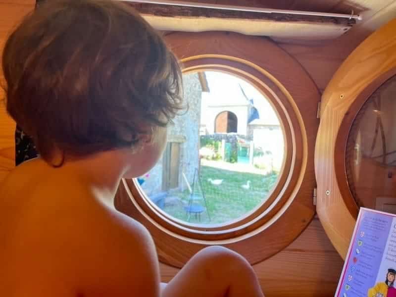 Cabane en bois avec vue ronde sur le jardin et des poules. Enfant contemplatif à lintérieur.