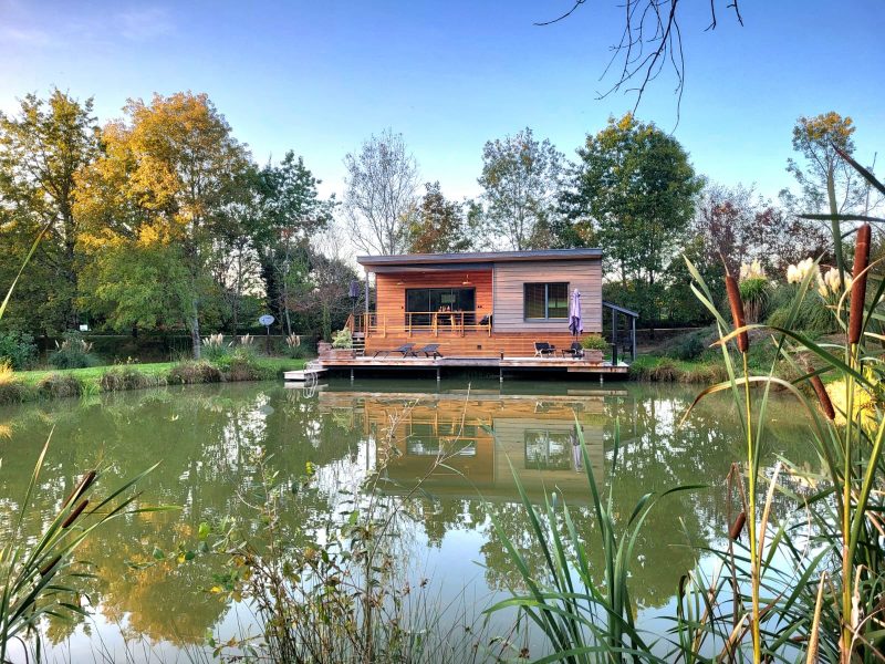 Cabane flottante en Aquitaine, entourée de verdure et reflétée dans leau.