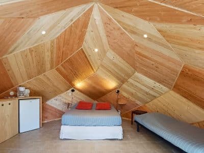 Hébergement insolite en Auvergne : chambre en bois avec un lit confortable et des murs géométriques.