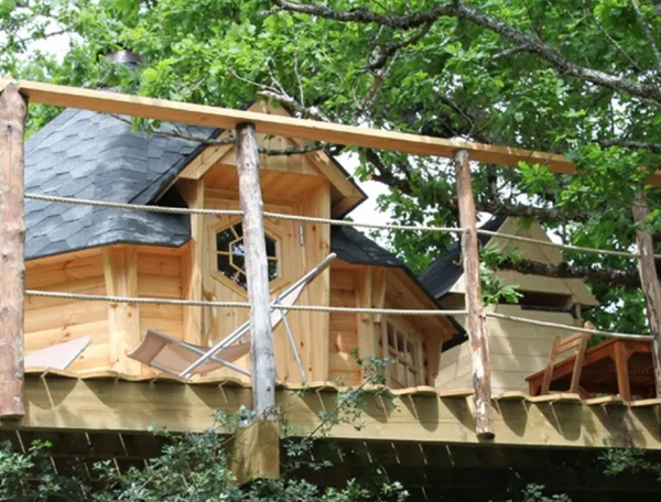 Cabane perchée dans les arbres, en bois, avec terrasse ensoleillée.