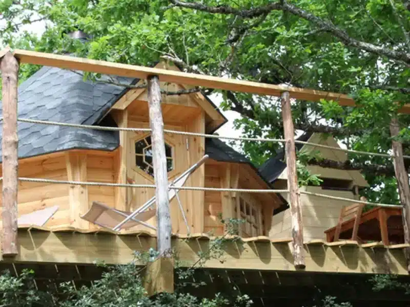 Cabane perchée dans les arbres, en bois, avec terrasse ensoleillée.