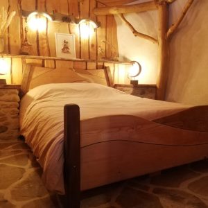 Chambre dhôtes chaleureuse avec lit en bois et murs en pierre.