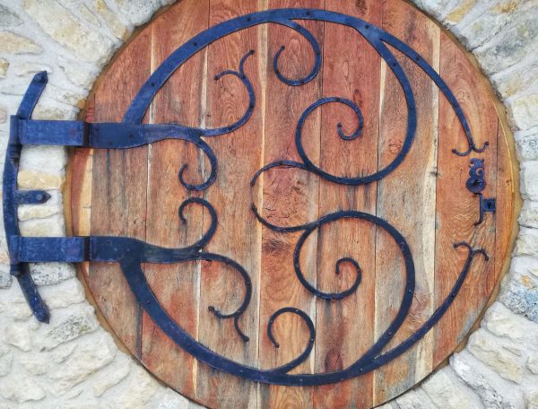 Porte en bois ronde dun gîte, ornée de ferronneries artistiques.