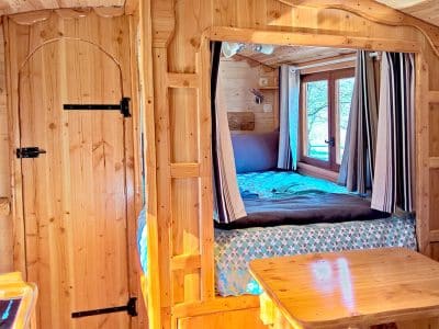 Cabane en bois chaleureuse avec lit douillet et fenêtres lumineuses.