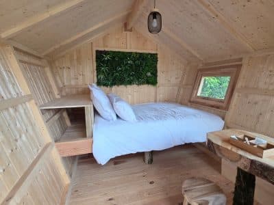 Cabane en bois avec lit douillet et mur végétal, idéale pour un séjour nature.