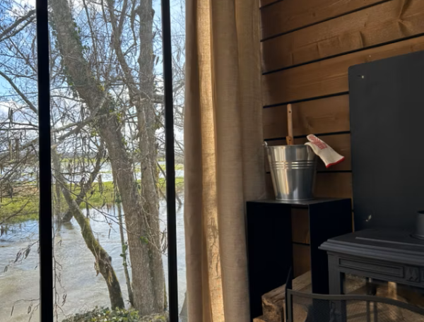 Hébergement insolite en bois avec vue sur la rivière et cheminée chaleureuse.
