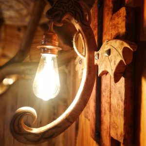 Applique en bois sculpté avec ampoule vintage dans un hébergement insolite en Nouvelle-Aquitaine.