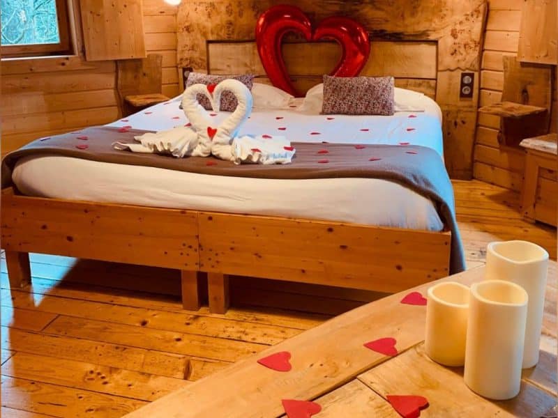 Chalet romantique en bois avec lit décoré de cœurs et ambiance chaleureuse.