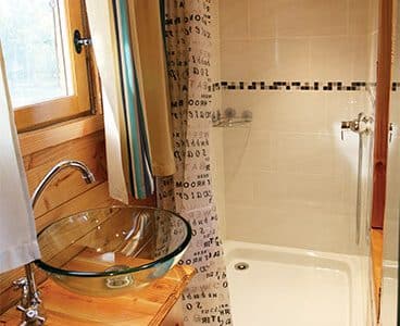 Salle de bain dun hébergement insolite en bois, avec douche et lavabo en verre.