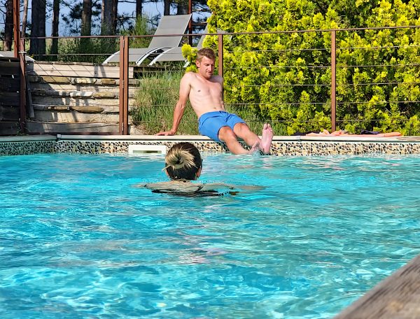 Hébergement avec piscine, un homme se détend au bord de leau sous un soleil radieux.