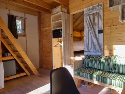 Cabane en bois cosy avec escalier, coin salon et vue sur la chambre.