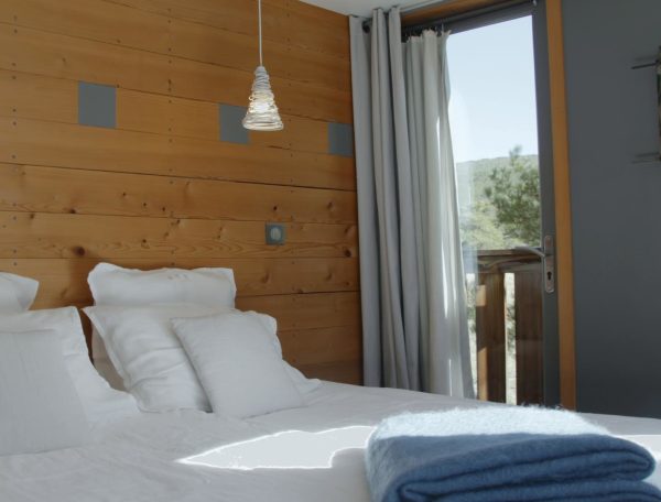 Chambre dhôtes moderne avec mur en bois et vue sur la nature. Draps blancs et plaid bleu.