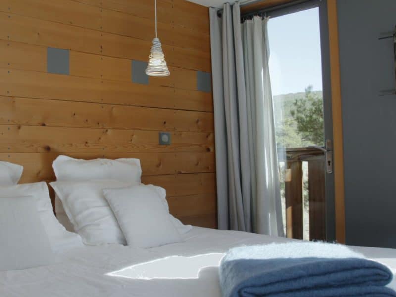 Chambre dhôtes moderne avec mur en bois et vue sur la nature. Draps blancs et plaid bleu.