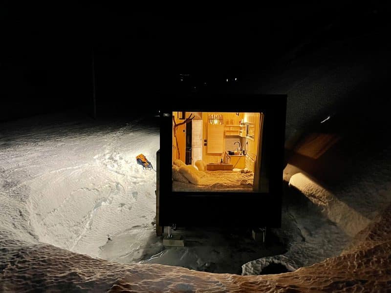 Cabane en bois lumineuse dans la neige, offrant un refuge chaleureux et cosy.