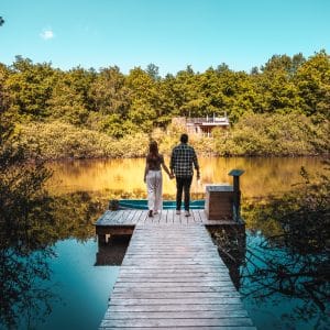Cabane au bord de leau, couple main dans la main sur un ponton en bois.