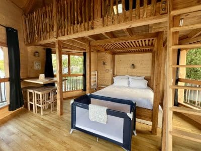 Cabane en bois spacieuse avec lit double et coin repas, lumineuse et chaleureuse.