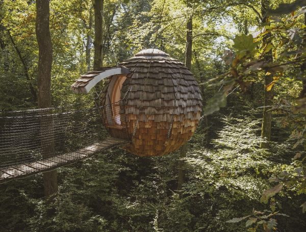 Cabane suspendue en bois, perchée dans les arbres, entourée de verdure luxuriante.