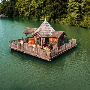 Cabane flottante en bois sur un lac, entourée de verdure luxuriante.