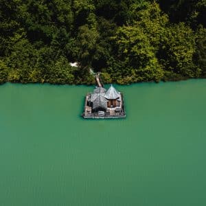 Cabane flottante sur un lac turquoise, entourée de verdure luxuriante.
